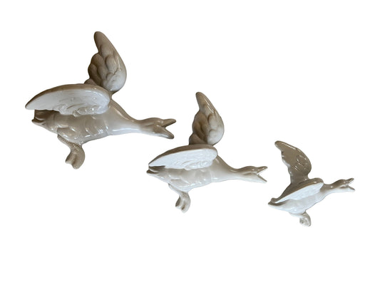 A SET OF THREE WHITE CERAMIC FLYING DUCKS, THE LARGEST 24 x 24cm.