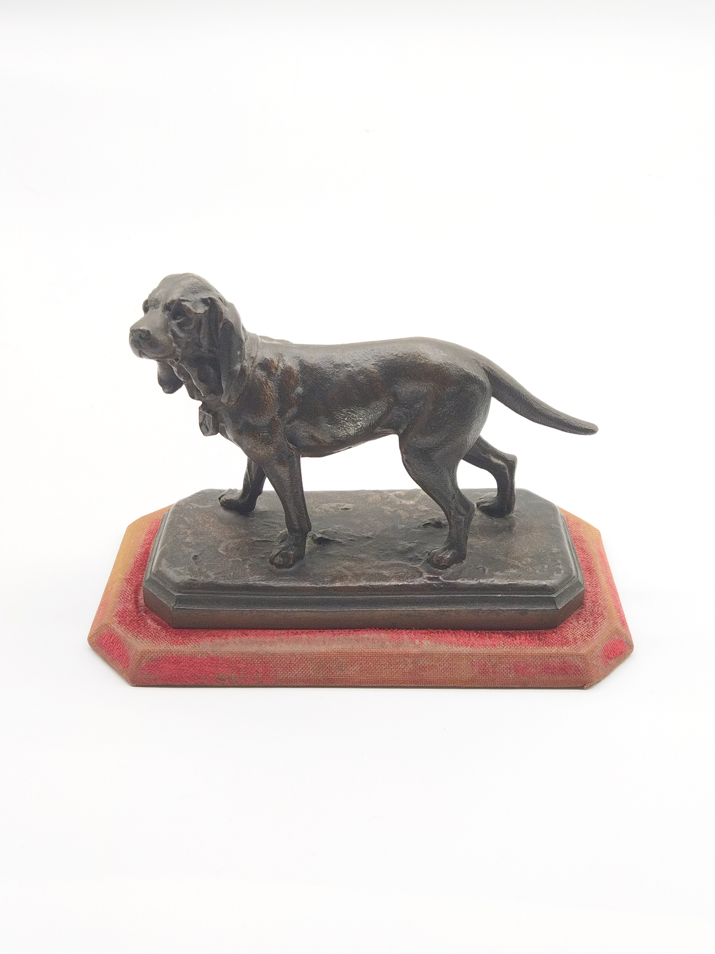 AN ANTIQUE BRONZE IN THE FORM OF A BLOODHOUND, TO A WORN RED VELVET BASE, 18 x 14 x 8cm.