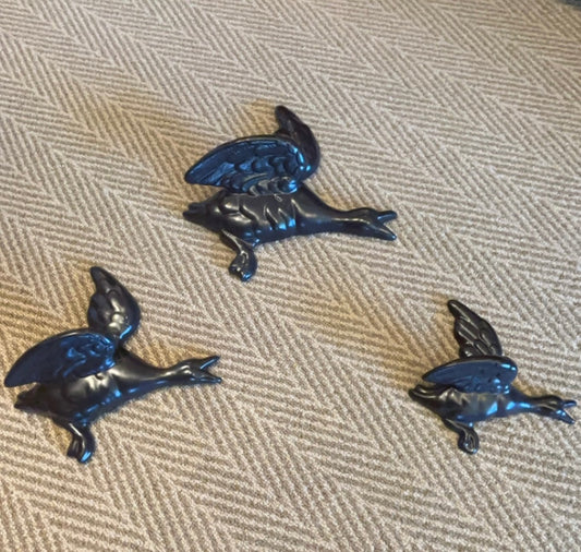 A SET OF THREE BLACK CERAMIC FLYING DUCKS