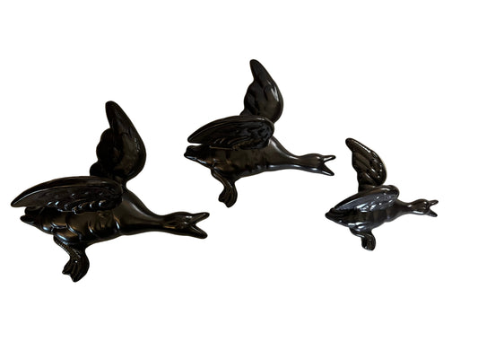 A SET OF THREE BLACK CERAMIC FLYING DUCKS, THE LARGEST 24 x 24cm.