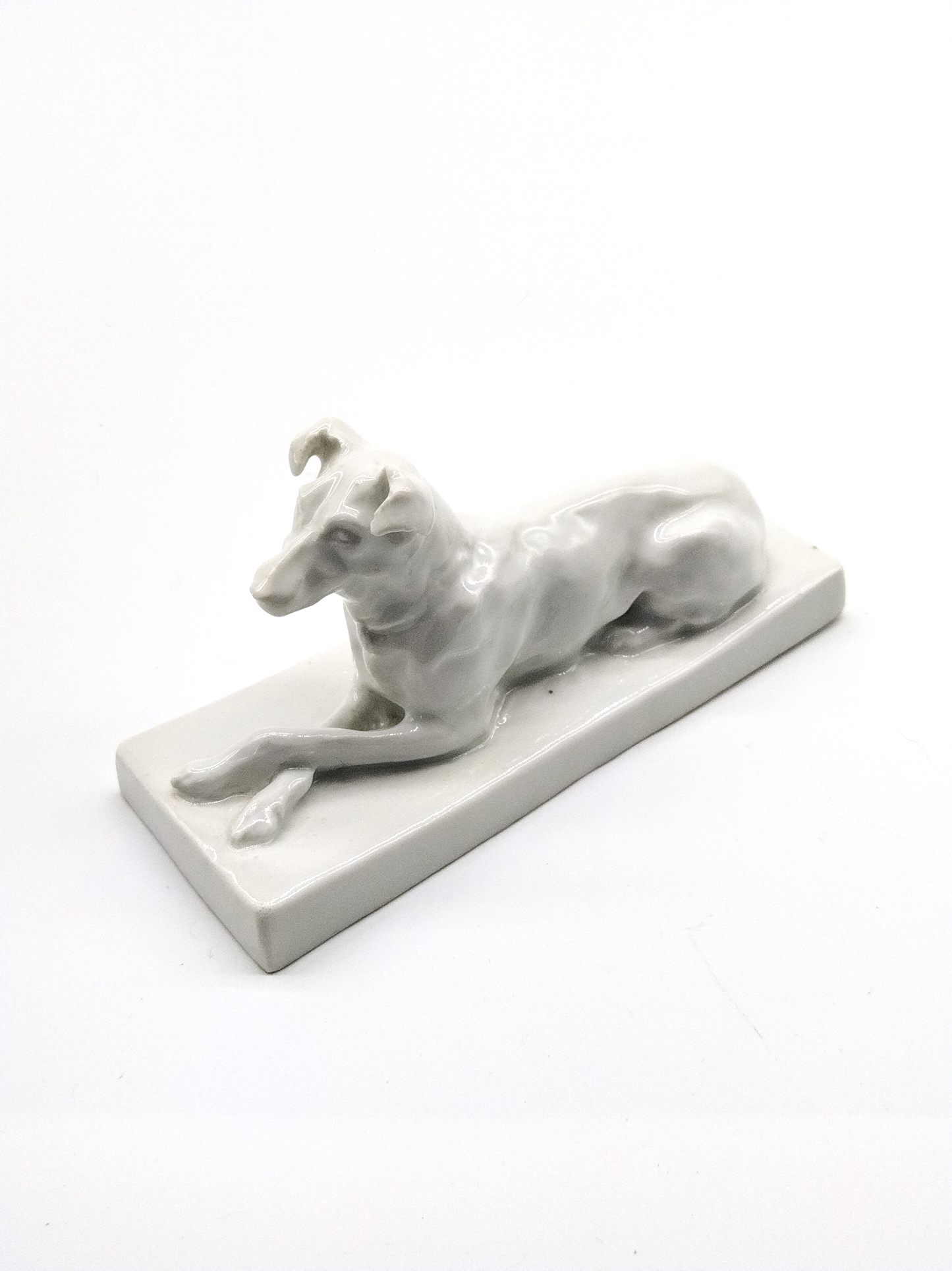 A GERMAN BANC-DE-CHINE RECLINING DOG PORCELAIN FIGURE, 17 x 6 x 10cm.